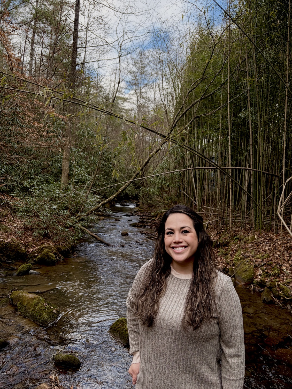 Fatima smiling by a stream in a bamboo forest
